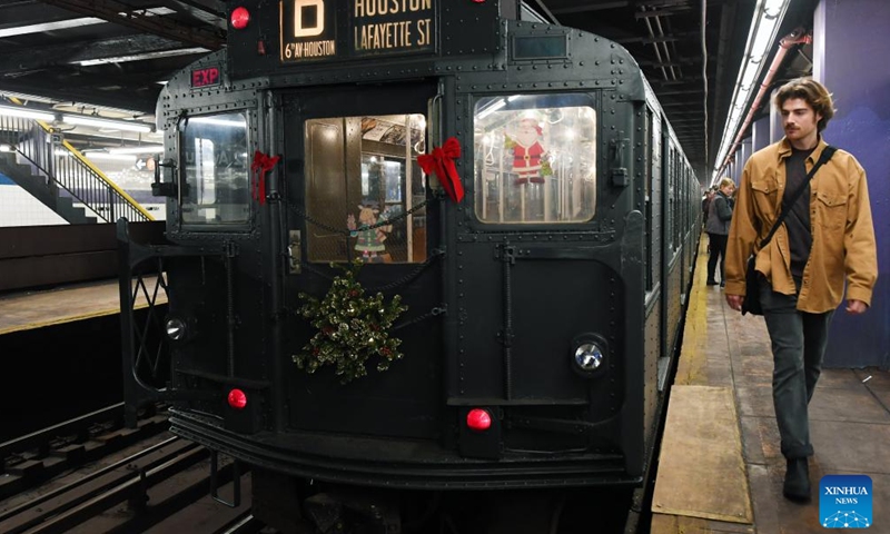 A man walks past the Holiday Nostalgia Train in New York, the United States, Dec. 2, 2023. A special subway train with eight cars entering service from 1932 to 1977 started its 2023 season on Saturday. This special subway train, with rattan seats, paddle ceiling fans, incandescent light bulbs, roll signs, and period advertisements, transports straphangers back in time between 2nd Avenue and 145th Street in Manhattan every Saturday in December. (Photo: Xinhua)