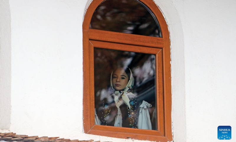 A girl of a traditional song and dance band watches performances during the White Flowers festival of traditions and customs at the Village Museum in Bucharest, capital of Romania, on Dec. 10, 2023. The festival is organized annually with the aim of presenting Christmas and New Year traditions to the public. (Photo: Xinhua)