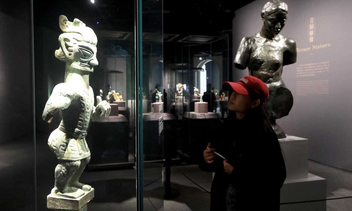 A visitor examines the Bronze Standing Figure Wearing a Skirt, an artifact unearthed from the Sanxingdui Ruins, at the exhibition Glory of Bronze Civilization: A Dialogue between Sanxingdui and Auguste Rodin across Space and Time at the Shanghai University Museum on December 14, 2023. Photo: Chen Xia/GT