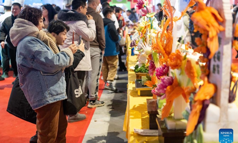 Tourists take photos of carvings made of vegetables and fruits during a food festival in Harbin, northeast China's Heilongjiang Province, Jan. 20, 2024. (Xinhua/Xie Jianfei)