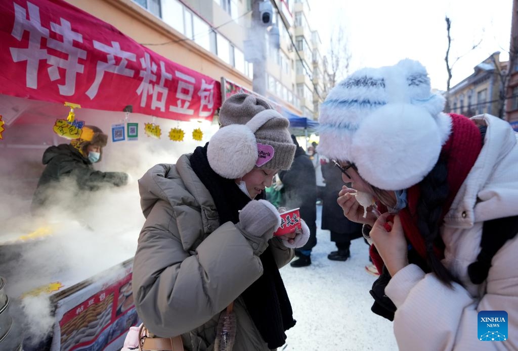 Tourists taste sticky steamed buns stuffed with bean paste at the Hongzhuan Morning Market in Harbin, northeast China's Heilongjiang Province, Jan. 22, 2024. Harbin's morning markets, known for their diverse offerings at reasonable prices, have been a hot spot for tourists.The morning market on Hongzhuan Street has been one of the first local morning markets to gain fame recently. Food stalls serving steaming local breakfast dishes are bustling with tourists eager to taste local delicacies.(Photo: Xinhua)