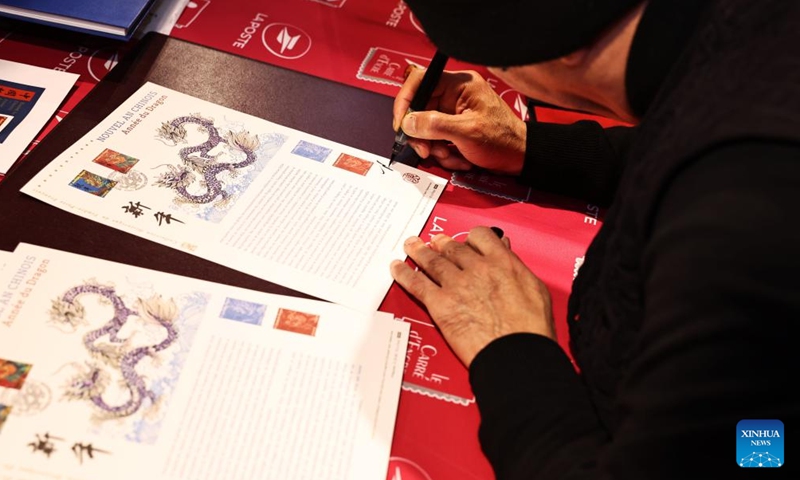 Chen Jianghong, a French artist of Chinese origin who designed a pair of stamps to celebrate the upcoming Chinese Lunar New Year, signs for a philatelist in Paris, France, Jan. 26, 2024. France's La Poste Group unveiled a pair of stamps on Friday to celebrate the upcoming Chinese Lunar New Year, the Year of the Dragon.(Xinhua/Gao Jing)