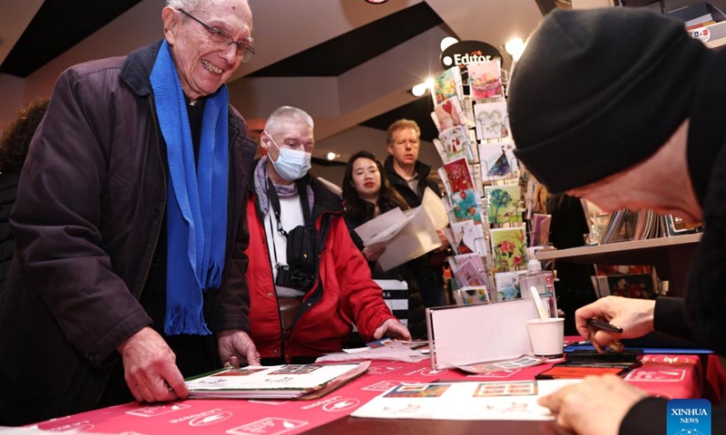Chen Jianghong, a French artist of Chinese origin who designed a pair of stamps to celebrate the upcoming Chinese Lunar New Year, signs for a philatelist in Paris, France, Jan. 26, 2024. France's La Poste Group unveiled a pair of stamps on Friday to celebrate the upcoming Chinese Lunar New Year, the Year of the Dragon.(Xinhua/Gao Jing)