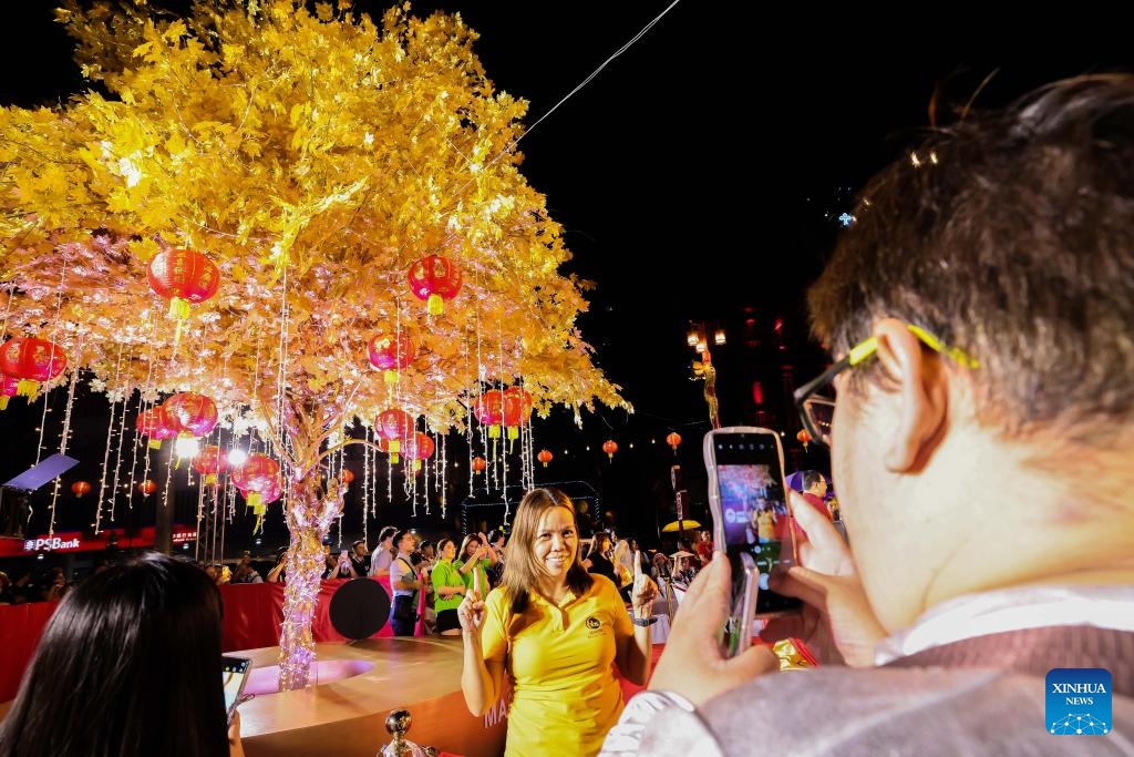 A woman poses for a photo with the prosperity tree during its lighting ceremony to celebrate the upcoming Chinese Lunar New Year at Chinatown in Manila, the Philippines, on Feb. 1, 2024.(Photo: Xinhua)