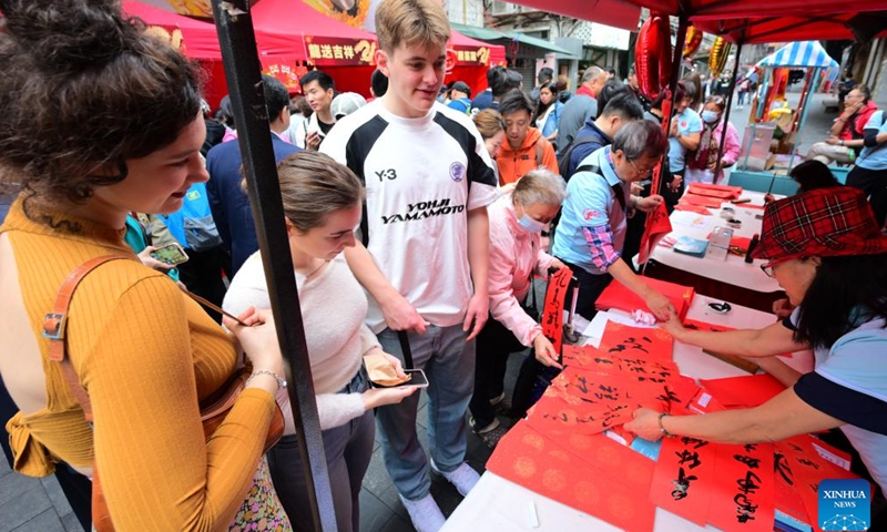Overseas students watch as artists write Chinese calligraphy during an event celebrating the upcoming Chinese New Year at the Temple Street in south China's Hong Kong, Feb. 4, 2024. (Xinhua/Zhu Wei)