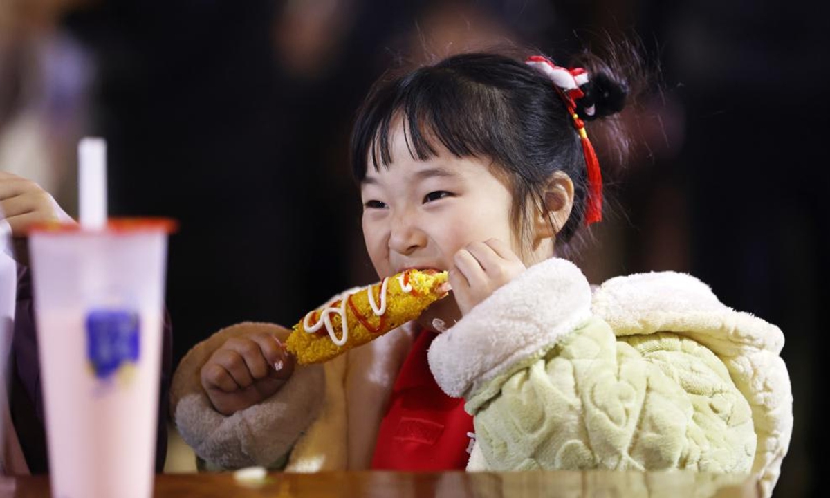 A girl tastes a snack on a food street in Tancheng County of Linyi City, east China's Shandong Province, Feb. 12, 2024. People across the country immersed themselves in the festive atmosphere of the Chinese New Year by enjoying traditional food and local snacks. (Photo by Zhang Chunlei/Xinhua)