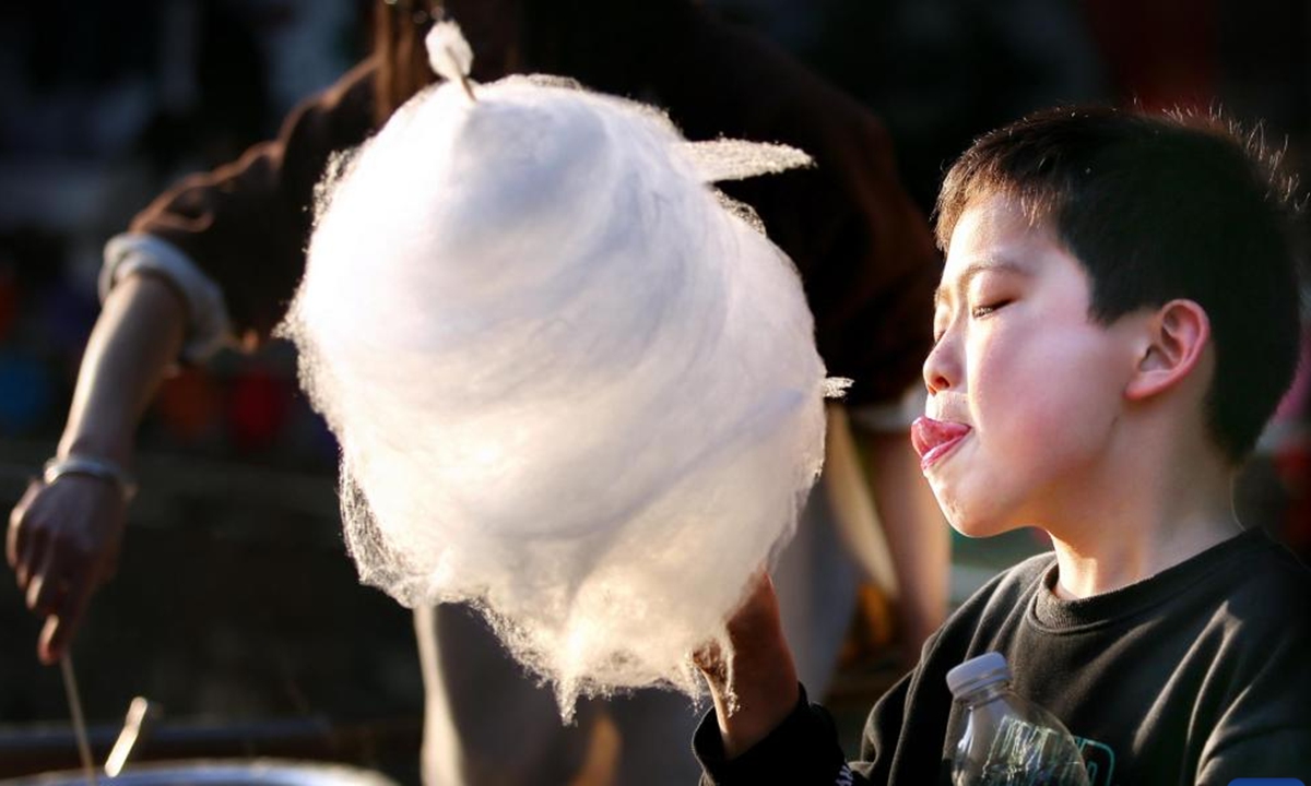 A boy eats cotton candy on a street in Shunde District of Foshan, south China's Guangdong Province, Feb. 12, 2024. People across the country immersed themselves in the festive atmosphere of the Chinese New Year by enjoying traditional food and local snacks. (Photo by Huang Jiming/Xinhua)