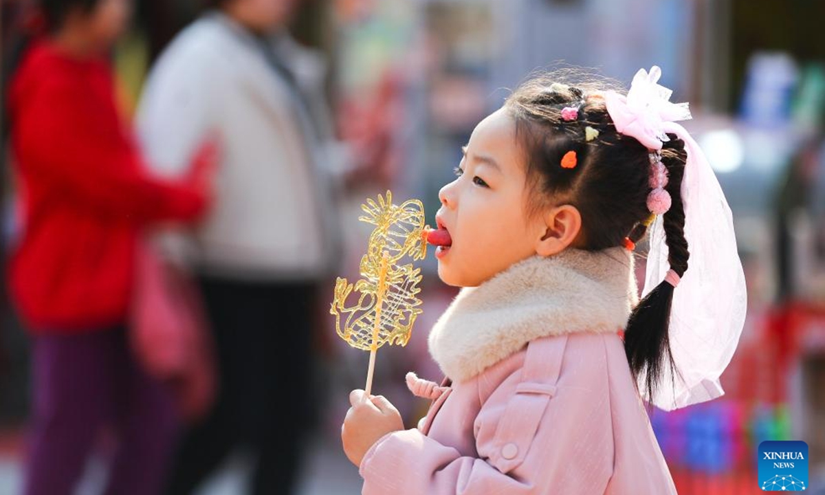 A girl tastes a sugar painting at a park in Tengzhou City, east China's Shandong Province, Feb. 13, 2024. People across the country immersed themselves in the festive atmosphere of the Chinese New Year by enjoying traditional food and local snacks. (Photo by Li Zhijun/Xinhua)