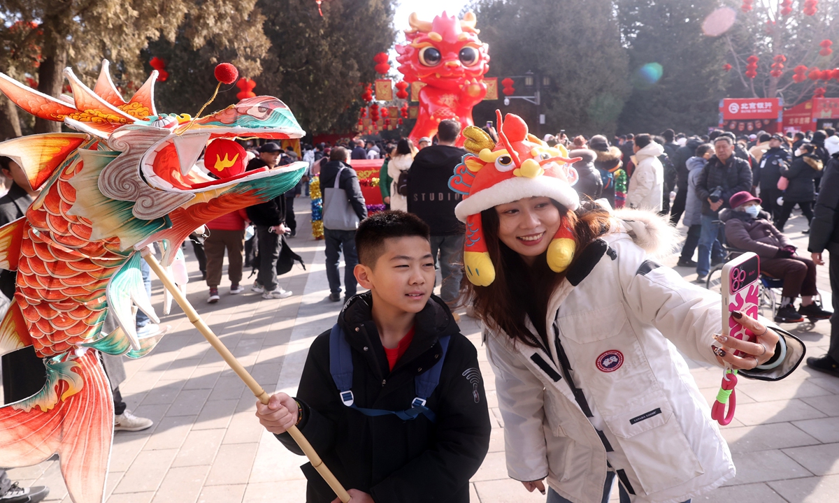 Tourists take a photo with a dragon lantern against the backdrop of Longlong, the zodiac mascot of the Ditan temple fair, at Ditan Park in Beijing on February 11, 2024. Photo: VCG