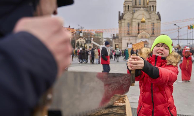 A girl participates in a wood sawing game in the central square in Vladivostok, Russia, March 17, 2024. On Sunday, the Russian Far East city of Vladivostok celebrates Maslenitsa, bidding winter farewell and welcoming spring. Locals engage in traditional games and enjoy blini in the central square. (Photo by Guo Feizhou/Xinhua)