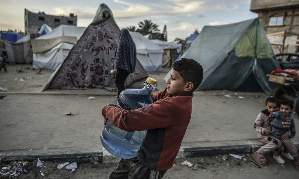 A child carries a water bottle at makeshift tents set up near the border of Egypt as Israeli attacks continue on March 09, 2024, in Rafah, Gaza. Photo: VCG