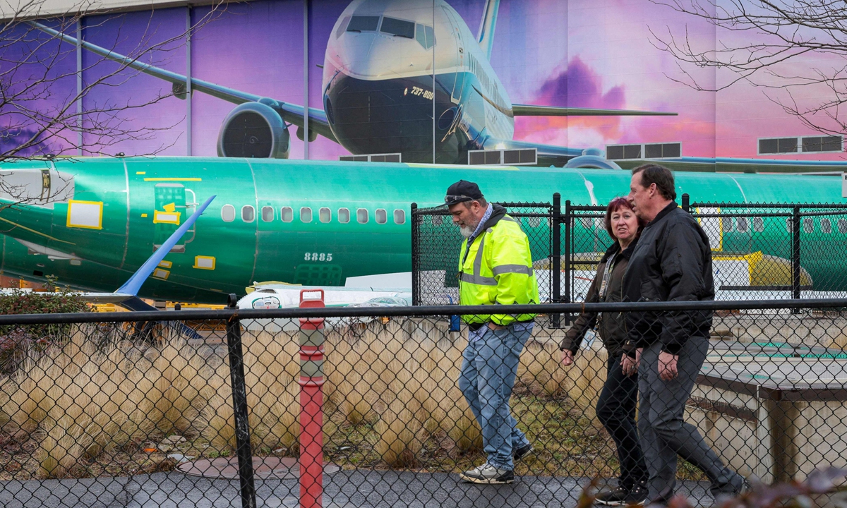 Boeing workers walk past an unpainted 737 fuselage and an image of a Boeing 737-800 aircraft on the first day of a 