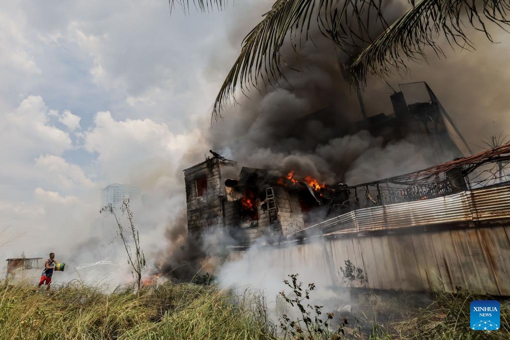 A resident tries to put out the flame at the site of a fire accident in Quezon City, the Philippines, March 19, 2024. Some 400 families were affected by a fire accident that took place in Quezon City on Tuesday, according to local officials.(Photo: Xinhua)