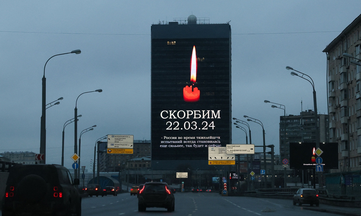 Des voitures passent devant un écran publicitaire sur la façade d’un bâtiment affichant l’image d’une bougie allumée et le slogan Deuil 22.03.24 à Moscou, en Russie, le 23 mars 2024, un jour après une attaque terroriste contre l’hôtel de ville de Crocus dans la banlieue de Moscou. Crédit photo : VCG 