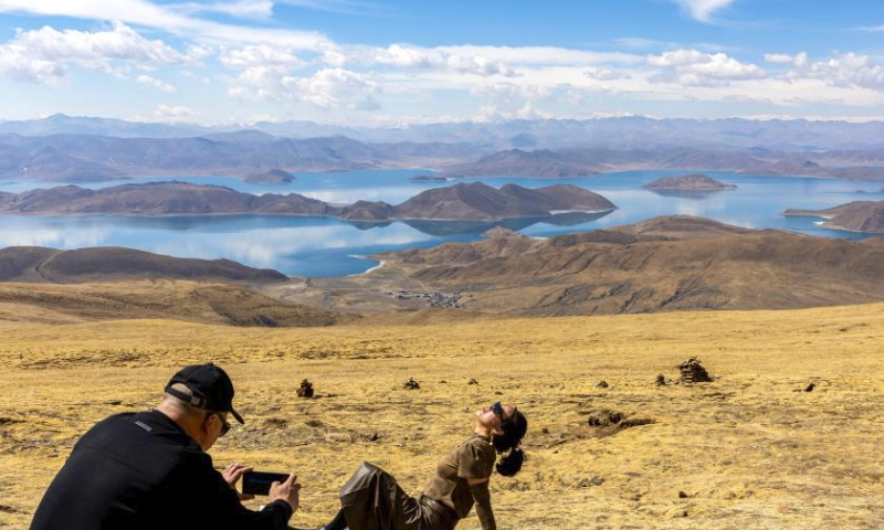 A tourist poses for a photo with the Yamzbog Yumco Lake in the background in southwest China's Xizang Autonomous Region, April 5, 2024. (Xinhua/Jiang Fan)