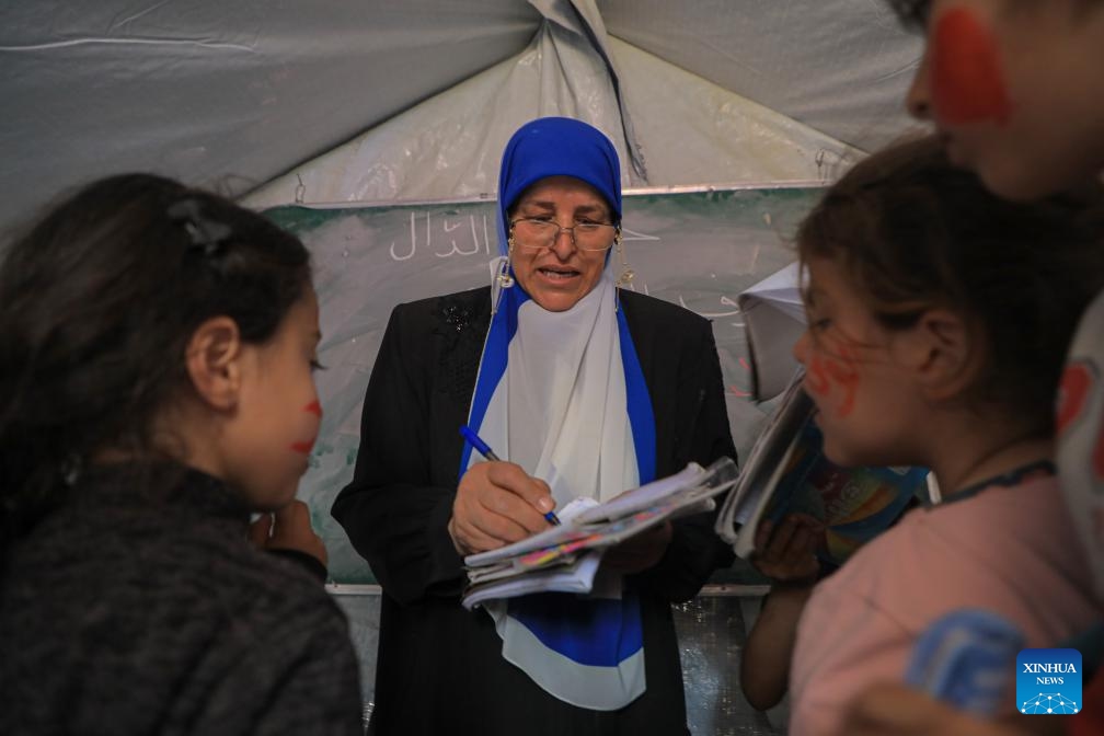 A Palestinian teacher teaches children at a temporary classroom in the southern Gaza Strip city of Rafah, March 27, 2024. The heavy bombardment against Gaza by Israel has resulted in direct hits on 212 schools within the enclave, according to analysis partnered with the United Nations released on Wednesday. Satellite images have shown that at least 53 schools have been completely destroyed since the conflict began on Oct. 7, 2023.(Photo: Xinhua)