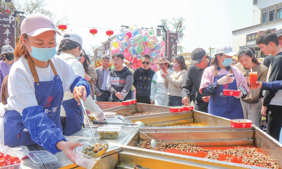 Visitors taste luosi, a kind of river snail, and other local specialties at a market on March 31, 2024 in Jiangba township of Huai'an city, East China's Jiangsu Province. On March 30 and 31, the town held a food fair, attracting an average of 50,000 tourists per day. The town's daily sales of luosi from March to May each year amounted to about 10,000 kilograms, and the industry's output value exceeded 100 million yuan ($13.85 million). Photo: VCG
