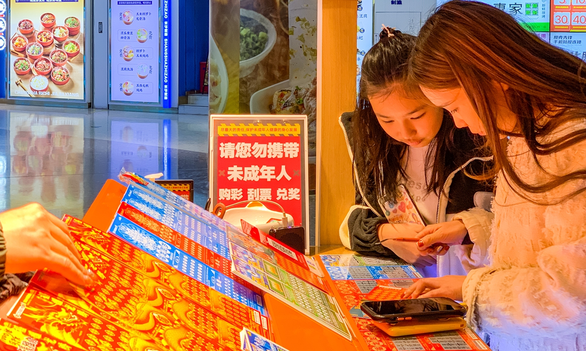 Two scratch ticket enthusiasts examine their tickets at a lottery ticket booth. Photo: VCG