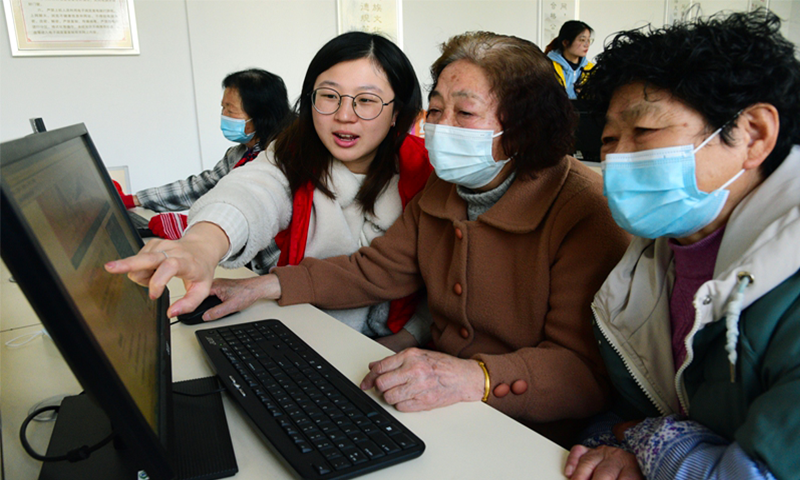 Volunteers from Jiangsu University help the elderly browse news about the two sessions online in Zhenjiang, East China's Jiangsu Province on March 8, 2022. Older people are using computers and smartphones to read about old-age security, medical care policies, and services for the elderly discussed at the two sessions. Photo: VCG