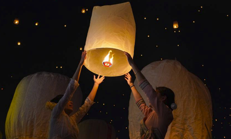 People fly Kongming lanterns, a kind of small hot-air paper balloon, by the Lancang River in Jinghong City, southwest China's Yunnan Province, April 13, 2024, to celebrate the New Year of the calendar of the Dai ethnic group. (Xinhua/Wang Jingyi)