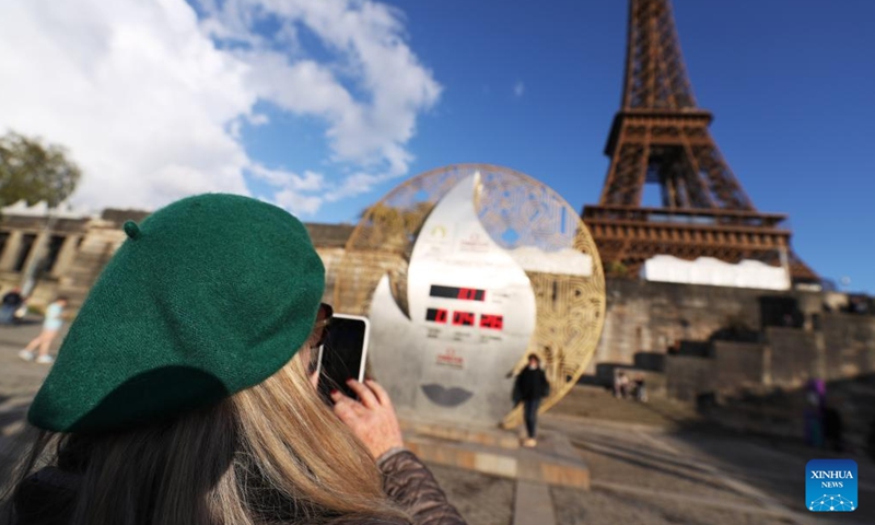 A tourist poses for photos with a countdown clock for the Paris 2024 Olympic Games in front of the Eiffel Tower in Paris, France, April 16, 2024.(Photo: Xinhua)