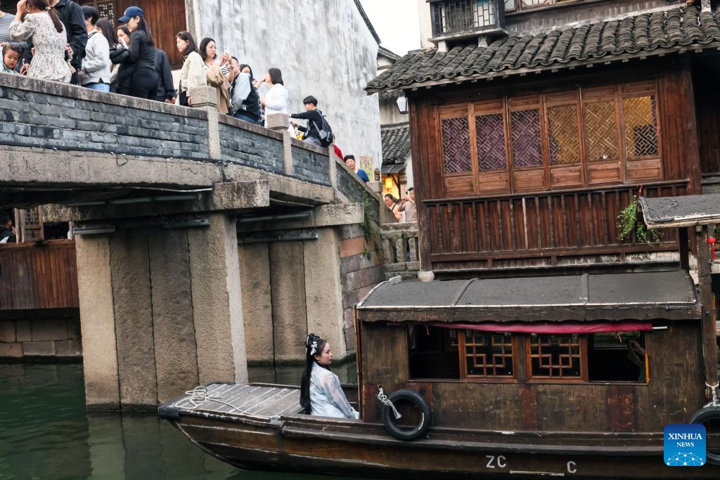 Tourists are seen on a stone bridge while a woman donning traditional attire visits on a rowing boat in water town Wuzhen in Jiaxing City, east China's Zhejiang Province, April 11, 2024. Located in east China's Zhejiang Province, the waterside city Jiaxing is renowned for tourist destinations Nanhu Lake and Wuzhen.(Photo: Xinhua)