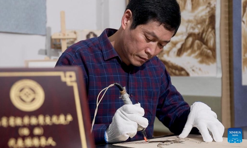 This undated photo shows Li Zhe making a wooden pyrography at a studio of Nanyang Pyrography Factory in Nanyang City, central China's Henan Province.