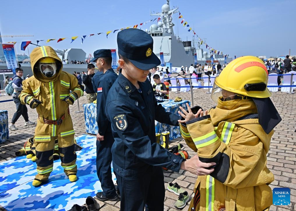 Visitors try on fireproof suits at the pier 3 in Qingdao Port of Qingdao, east China's Shandong Province, April 21, 2024. The Chinese People's Liberation Army Navy holds open day events in multiple coastal cities including Qingdao around April 23 to mark the 75th anniversary of its founding.(Photo: Xinhua)
