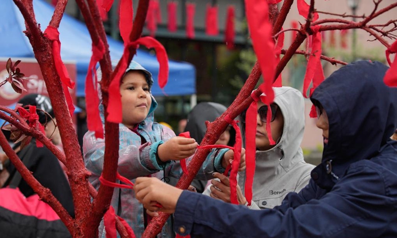 People tied red ribbons on a tree during the Red Dress Day ceremony in New Westminster, British Columbia, Canada, on May 5, 2024. May 5 is the National Day of Awareness for Missing and Murdered Indigenous Women and Girls, also known as Red Dress Day, in Canada. Photo: Xinhua
