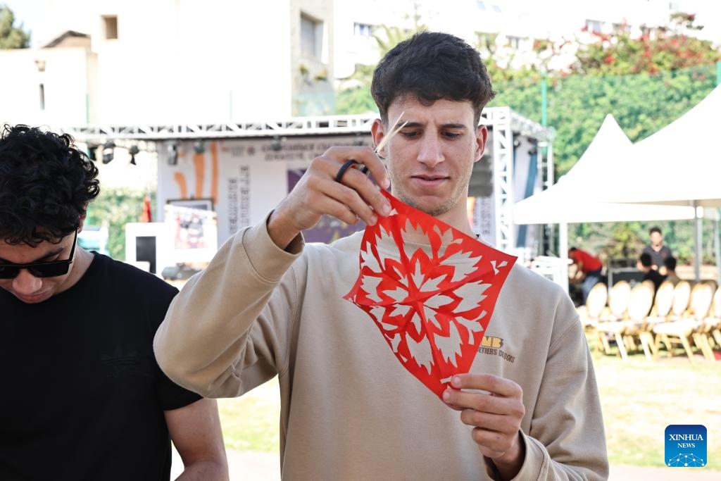 A man tries the Chinese paper-cutting at the 20th world culture festival in Rabat, Morocco, May 8, 2024. The 20th world culture festival of the Rabat School of Mines kicked off here on Wednesday. Chinese paper-cutting, Lu Ban Lock and painting of opera facial mask were welcomed by Moroccan students.(Photo: Xinhua)