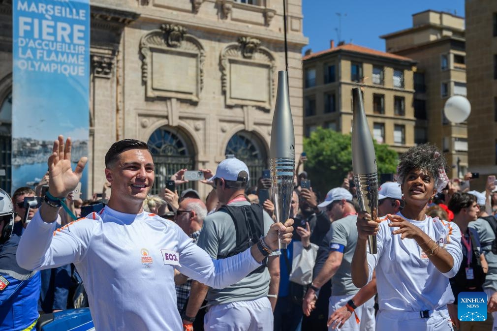 Dancer Maryam Kaba (R) passes the Olympic Torch to local firefighter Matthieu Gudet during the relay of the Olympic flame of Paris 2024 in Marseille, France, May 9, 2024.(Photo: Xinhua)
