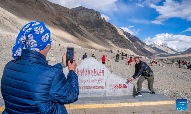 Ekke Kok, a tourist from Canada, poses for photos with the monument to the elevation survey of Mount Qomolangma in southwest China's Xizang Autonomous Region, May 24, 2024. The Mount Qomolangma National Park has entered peak tourism season. In 2023, the scenic spot had received about 464,000 tourists, and saw its ticket revenue totaling 110 million yuan (about 15.2 million U.S. dollars). (Photo: Xinhua)