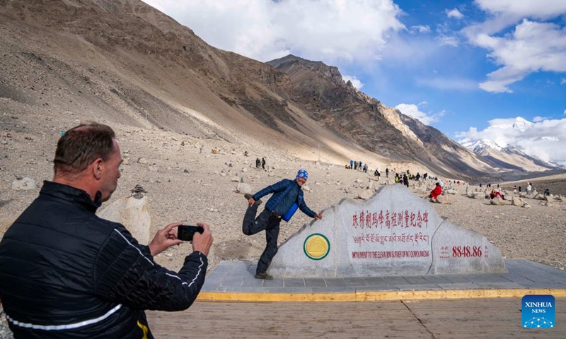 Rolf Ravnskov, a tourist from Denmark, poses for photos with the monument to the elevation survey of Mount Qomolangma in southwest China's Xizang Autonomous Region, May 24, 2024. The Mount Qomolangma National Park has entered peak tourism season. In 2023, the scenic spot had received about 464,000 tourists, and saw its ticket revenue totaling 110 million yuan (about 15.2 million U.S. dollars). (Photo: Xinhua)