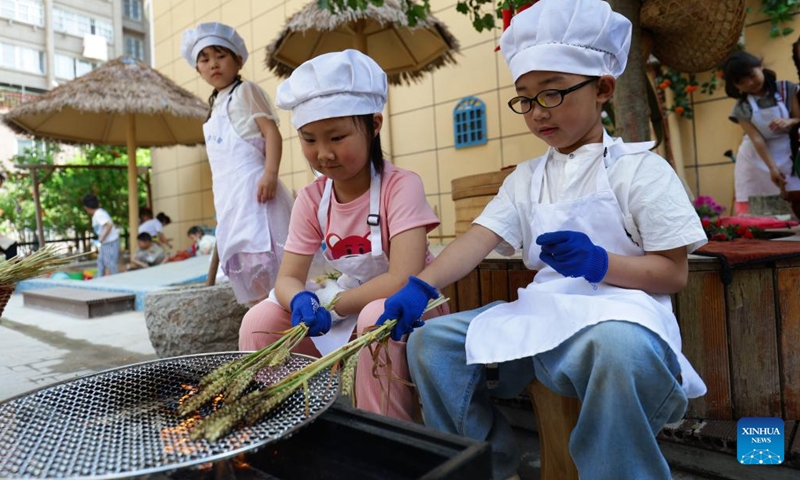Children roast ears of wheat at Xuhai Road Kindergarten in Xuzhou, east China's Jiangsu Province, May 23, 2024. In the city of Xuzhou, Xuhai Road Kindergarten produces an unconventional symphony featuring the rhythmic chopping of vegetables, the comforting sizzle of baking buns, and the gentle grind of the soybean milk milling process. (Photo: Xinhua)