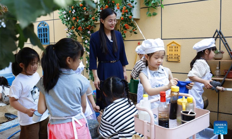 Zhang Qian (C), principal of Xuhai Road Kindergarten, attends a kitchen skill class with children at the kindergarten in Xuzhou, east China's Jiangsu Province, May 23, 2024. In the city of Xuzhou, Xuhai Road Kindergarten produces an unconventional symphony featuring the rhythmic chopping of vegetables, the comforting sizzle of baking buns, and the gentle grind of the soybean milk milling process. (Photo: Xinhua)