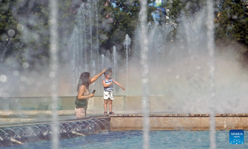 A woman arranges the hat for her child as they cool off at a public fountain amid a heatwave in Bucharest, Romania, June 22, 2024.(Photo: Xinhua)