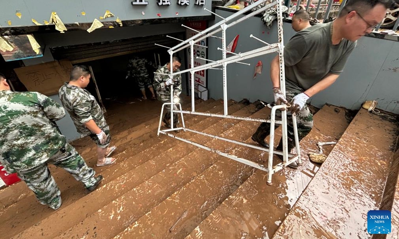 This photo taken by a mobile phone on June 23, 2024 shows people carrying items out of a flood-hit shop in Wuqiangxi Township of Yuanling County in central China's Hunan Province. Heavy rainfall hit Wuqiangxi Township on Saturday, triggering flood that impacted local residential area. Local authorities have carried out emergency response to minimize the impact of the extreme weather conditions. (Photo: Xinhua)