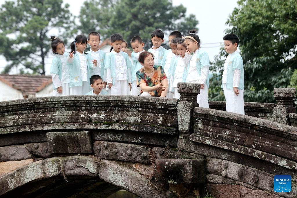 A volunteer tells the history of the Wanshan Bridge to a group of young visitors in Shebei Village of Xin'an Town, Deqing County, east China's Zhejiang Province, June 26, 2024. Deqing County is home to seven ancient stone bridges which are listed as major cultural heritage sites under state-level protection. (Photo: Xinhua)