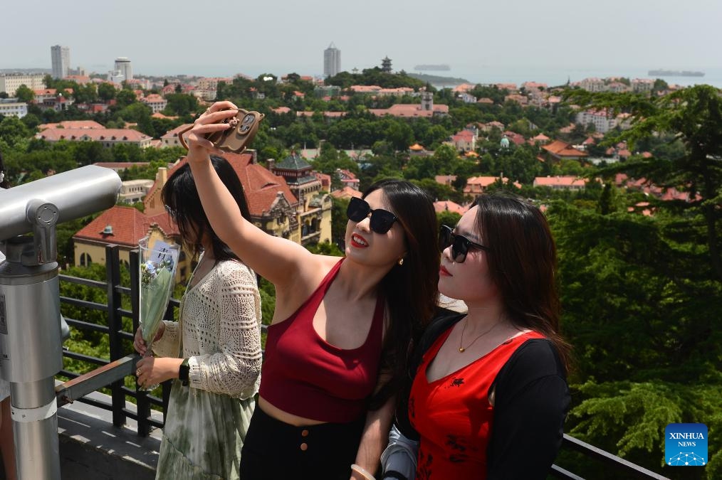 Tourists pose for a selfie at the Xinhao Mountain scenic spot in Qingdao, east China's Shandong Province, June 24, 2024. Tourism in Qingdao is heating up as domestic and foreign tourists come here to enjoy the coastal scenery and cool off in hot summer days.(Photo: Xinhua)
