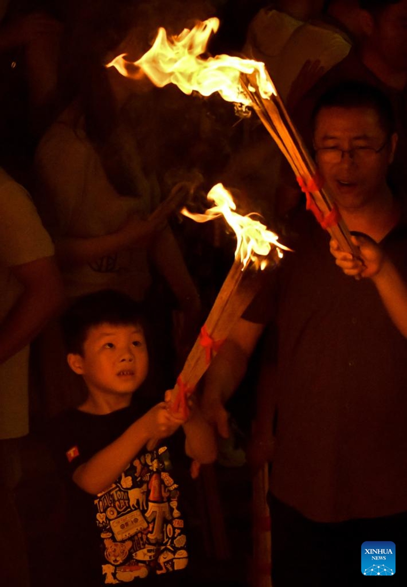 A child lights a torch at a torch festival in Chuxiong, southwest China's Yunnan Province, July 27, 2024. A torch festival of the Yi ethnic group kicked off here on Saturday. Photo: Xinhua