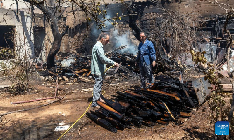 People spray water on wood ignited by wildfire in Chalandri, a suburb in northern Athens, Greece, on Aug. 13, 2024. (Photo: Xinhua)