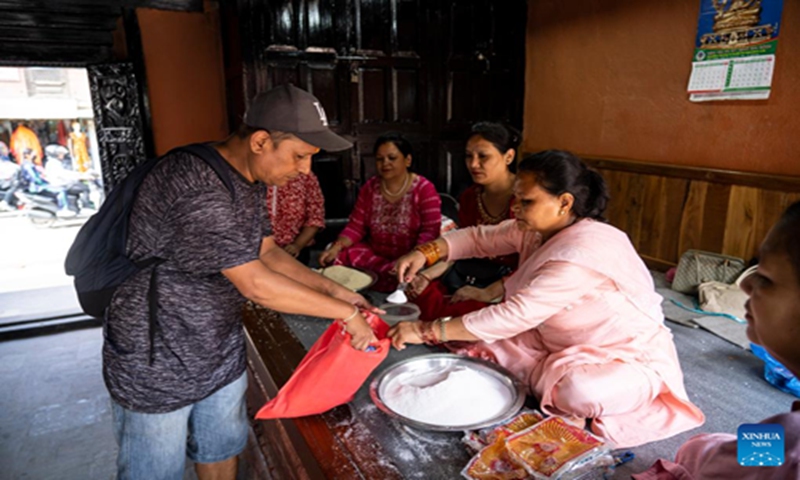 A Buddhist distributes an offering during the Pancha Dan festival in Lalitpur, Nepal, on Aug. 12, 2024. Pancha Dan, the festival of five summer gifts, is observed by the Buddhists by giving away five elements including wheat grains, rice grains, salt, money and fruit. (Photo: Xinhua)