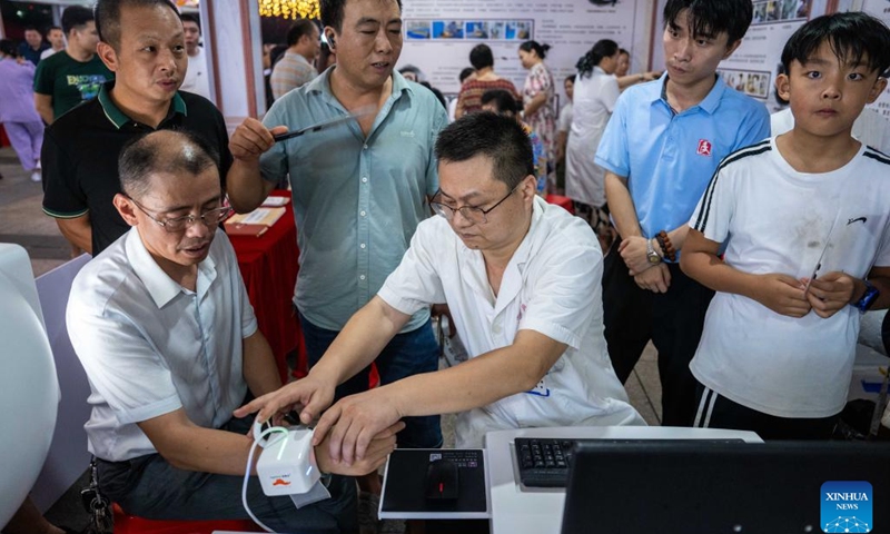 A medical worker (3rd R) takes a citizen's pulse with electric device at a night traditional Chinese medicine clinic in Changning City, central China's Hunan Province, Aug. 13, 2024. Local health bureau of Changning City has launched a night clinic, where traditional Chinese medical therapies and treatment services, such as acupuncture, moxibustion, remedial massage, etc., are available to residents for free. The clinic will last until Aug. 18.  (Photo: Xinhua)