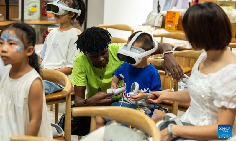 A volunteer helps a kid to put on VR device during a hands-on experience session at the Mali pavilion of a permanent exhibition hall of the China-Africa Economic and Trade Cooperation Promotion Innovation Demonstration Park in Changsha, central China's Hunan Province, Aug. 30, 2024. Various activities promoting youth communication between China and Africa were organized here during the summer vacation. With the help of African volunteers from local universities, Chinese students were able to feel the charm of African culture by learning traditional African dance, music, folk arts, and making immersive tours of African customs via VR devices. Photo: Xinhua