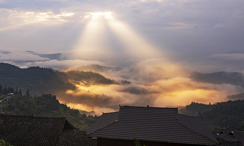Beams of light shine through the clouds, illuminating the mist-covered green mountains and traditional village homes in Southwest China's Guizhou Province, on September 18, 2024. Photo: VCG