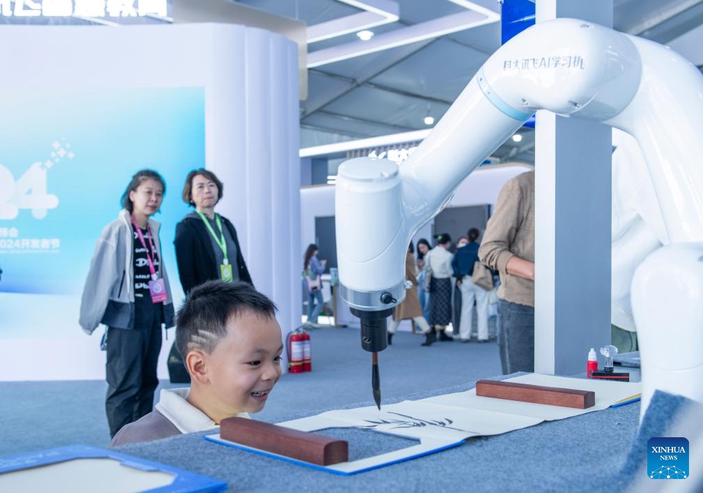 A boy looks at a robotic arm creating traditional Chinese painting at the 7th World Voice Expo in Hefei, east China's Anhui Province, Oct. 24, 2024. The 7th World Voice Expo and the iFlytek 1024 Global Developer Festival kicked off here on Thursday. The latest achievements and application of AI technology will be on display at the four-day event. (Photo: Xinhua)