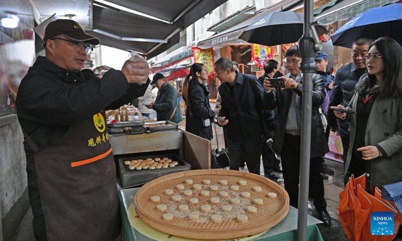 A merchant demonstrates the production process of sesame cake at the Youbu ancient town of Lanxi City, east China's Zhejiang Province, Dec. 5, 2024. Youbu ancient town, with a history of more than 1,300 years, is well known for its morning tea and photography elements and attracts a large number of tourists. (Photo: Xinhua)