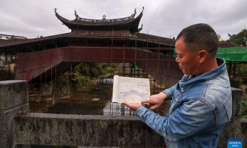 Zeng Jiakuai, a provincial-level inheritor of traditional design and practices for building Chinese wooden arch bridges, displays his hand-drawing of the structure of Xidong Bridge in front of the bridge in Taishun County of Wenzhou City, east China's Zhejiang Province, Dec. 11, 2024. (Photo: Xinhua)