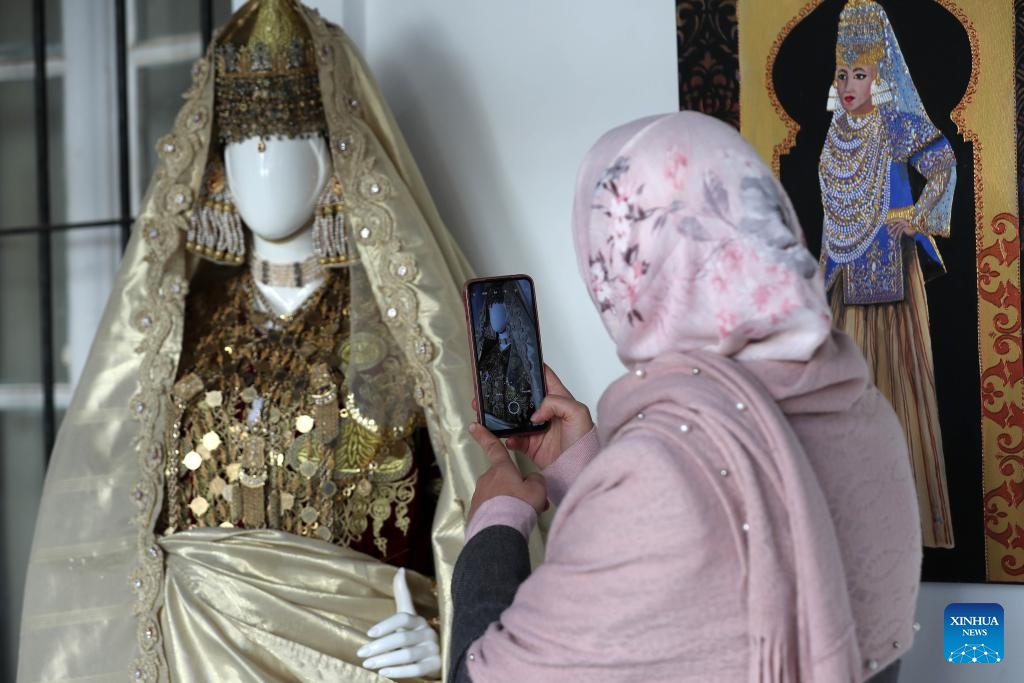 A visitor takes photos of a traditional women's attire displayed during an exhibition in Medea, Algeria, Dec. 12, 2024. (Photo: Xinhua)