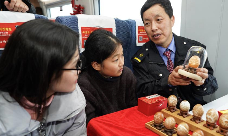 Wang Jian (R), inheritor of Luzhou eggshell carving technique, a provincial-level intangible cultural heritage in Anhui, shows his works on train C3685, east China's Anhui Province, Jan. 13, 2025. The Hefei branch of China Railway Shanghai Bureau Group Co., Ltd. organized railway staff to demonstrate local intangible cultural heritages on the train, adding festive atmosphere to the upcoming Spring Festival travel rush. (Xinhua/Du Yu)